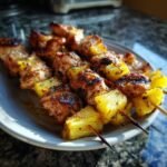 Nahaufnahme von gegrillten H&auml;hnchen- und Ananas-Spie&szlig;en, die auf einem Teller serviert werden.