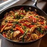 Knoblauch H&auml;hnchen Lo Mein in einer Pfanne mit Nudeln, H&auml;hnchenst&uuml;cken und rotem Paprika.