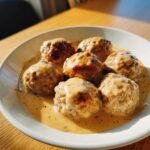 Nahaufnahme von Lightened Up Turkey Swedish Meatballs in cremiger So&szlig;e auf einem wei&szlig;en Teller.