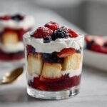 Nahaufnahme von Mixed Berry Mini Trifles im Glas mit Biskuit, Beeren und Sahne.