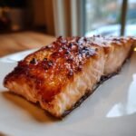 Nahaufnahme eines saftigen Pan Seared Salmon Filets mit karamellisierter Kruste auf einem wei&szlig;en Teller.