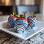 Nahaufnahme von patriotischen Schokoladen-Erdbeeren mit roten, wei&szlig;en und blauen Streifen und Streuseln auf einem wei&szlig;en Teller.