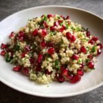 Nahaufnahme eines Pomegranate Quinoa Salat mit leuchtend roten Granatapfelkernen und gehackter Petersilie.