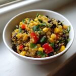 Nahaufnahme eines Quinoa Southwestern Salad mit Mais, schwarzen Bohnen und roter Paprika in einer wei&szlig;en Sch&uuml;ssel.