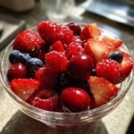 Nahaufnahme einer Sch&uuml;ssel mit rotem Fruchtsalat Sommergl&uuml;ck, darunter Erdbeeren, Himbeeren und Kirschen.