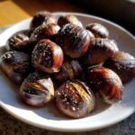 Ger&ouml;stete Esskastanien mit grobem Salz und Pfeffer auf einem wei&szlig;en Teller.