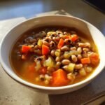 Nahaufnahme einer wei&szlig;en Sch&uuml;ssel mit Black Eyed Pea Soup, gef&uuml;llt mit Augenbohnen, Karottenw&uuml;rfeln und Sellerie.