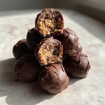 Stapel von schokoladen&uuml;berzogenen Bourbon Balls, zwei davon angeschnitten, um die F&uuml;llung zu zeigen.