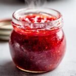 Nahaufnahme eines Glases mit frisch gekochter, dampfender Erdbeer-Rhabarber-Marmelade.