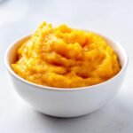 Nahaufnahme von leuchtend orangefarbenem Slow Cooker Pumpkin Puree in einer wei&szlig;en Sch&uuml;ssel.