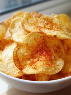 Nahaufnahme von knusprigen Air Fryer Kartoffelchips, bestreut mit rotem Paprikapulver, in einer weißen Schüssel.