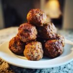 Ein Haufen saftiger Air Fryer Meatballs, goldbraun und gl&auml;nzend, gestapelt auf einem wei&szlig;en Teller.