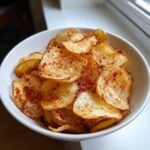 Eine wei&szlig;e Sch&uuml;ssel gef&uuml;llt mit knusprigen, goldbraunen Air Fryer Potato Chips, bestreut mit rotem Paprikapulver.