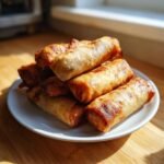 Stapel goldbrauner, knuspriger Air Fryer Spring Rolls auf einem wei&szlig;en Teller.
