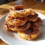 Stapel frittierter Apple Rings, bestreut mit Zimt und Zucker, auf einem wei&szlig;en Teller.