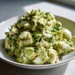 Nahaufnahme von cremigem Avocado Chicken Egg Salad mit Ei-St&uuml;cken und Kr&auml;utern in einer Schale.