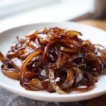 Nahaufnahme von gl&auml;nzenden, dunkelbraunen Balsamico Karamelisierte Zwiebeln auf einem wei&szlig;en Teller.