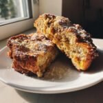 Zwei H&auml;lften Banana Bread Stuffed French Toast, best&auml;ubt mit Puderzucker, auf einem wei&szlig;en Teller.