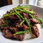 Nahaufnahme von saftigem Beef Bulgogi in dunkler So&szlig;e, garniert mit gr&uuml;nen Fr&uuml;hlingszwiebeln und Sesam, serviert auf wei&szlig;em Reis.