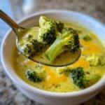 Ein L&ouml;ffel mit gro&szlig;en Brokkolir&ouml;schen in cremiger Broccoli Cheese Soup, nahaufnahme.