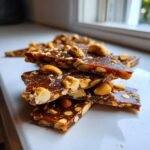 Gestapelte St&uuml;cke von Cashew-Haselnuss Toffee Bark mit karamellisiertem Glanz und ganzen N&uuml;ssen.