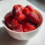 Nahaufnahme von leuchtend roten Champagner Erdbeeren, bestreut mit Zuckerkristallen, in einer wei&szlig;en Schale.