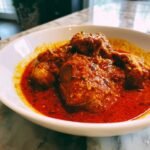 Nahaufnahme von saftigen H&auml;hnchenst&uuml;cken in einer tiefroten, w&uuml;rzigen Sauce: Chicken Rogan Josh.