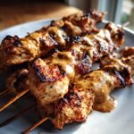 Gegrillte St&uuml;cke Chicken Satay auf Holzspie&szlig;en, &uuml;bergossen mit cremiger Erdnussso&szlig;e.