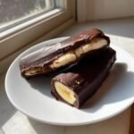 Zwei Chocolate Covered Frozen Bananas auf einem wei&szlig;en Teller, einer davon angeschnitten.