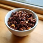 Nahaufnahme von knusprigem Chocolate Granola mit N&uuml;ssen und Schokost&uuml;ckchen in einer wei&szlig;en Sch&uuml;ssel.