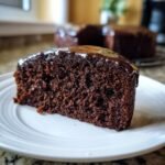 Nahaufnahme eines saftigen St&uuml;cks Chocolate Kahlua Cake mit dunkler Schokoladenglasur auf einem wei&szlig;en Teller.