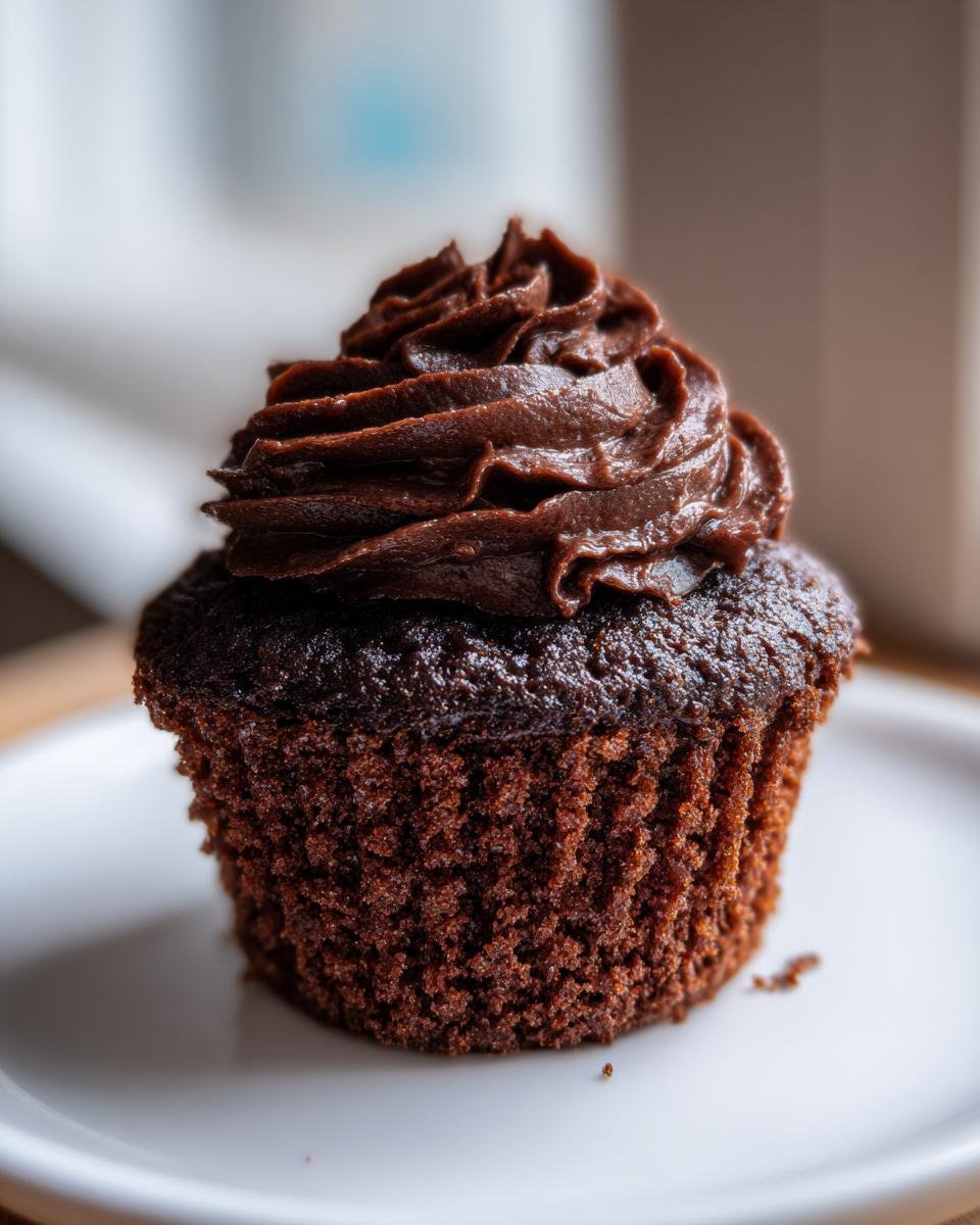 Nahaufnahme eines dunklen Chocolate Sweet Potato Cupcakes mit reichhaltigem Schokoladen-Frosting auf einem wei&szlig;en Teller.