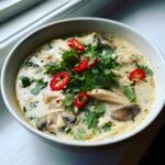 Nahaufnahme einer Sch&uuml;ssel mit cremiger Thai Chicken Soup, garniert mit frischem Koriander und roten Chiliringen.