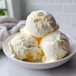 Drei Kugeln cremiges Cottage Cheese Ice Cream in einer wei&szlig;en Schale auf Marmor.