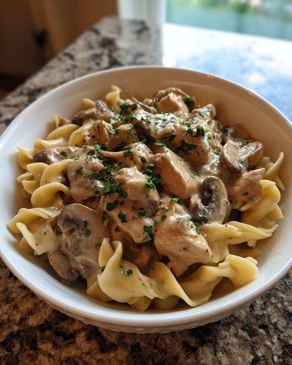 Nahaufnahme von Crock Pot Chicken Stroganoff mit cremiger Soße, Pilzen und Petersilie über Eiernudeln.