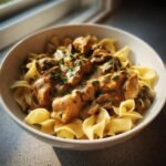 Nahaufnahme von Crock Pot Chicken Stroganoff mit cremiger So&szlig;e und Petersilie auf Bandnudeln in einer wei&szlig;en Sch&uuml;ssel.