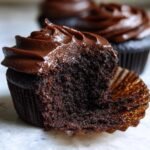 Nahaufnahme eines angeschnittenen Devils Food Cupcakes mit saftigem Inneren und reichhaltiger Schokoladen-Frosting.