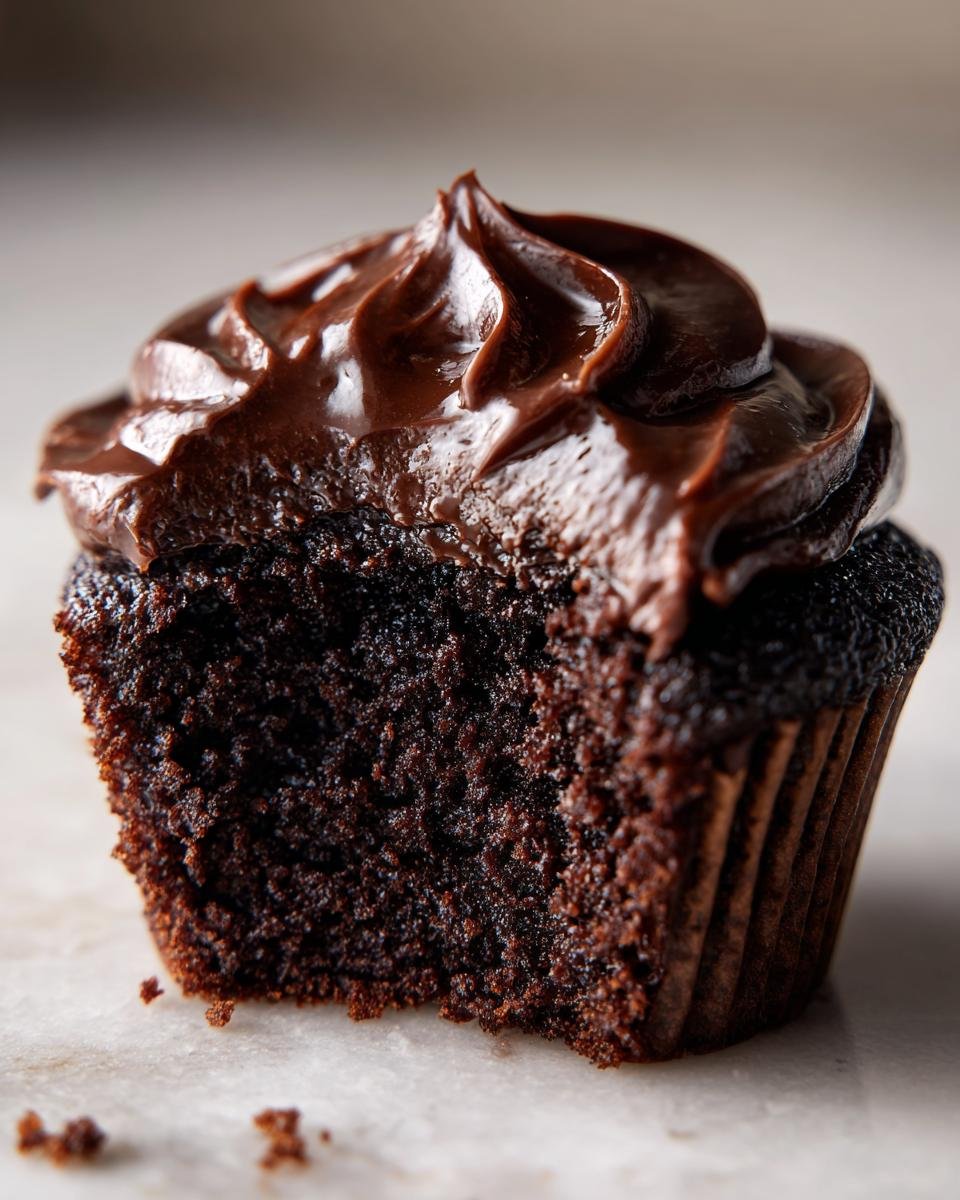 Nahaufnahme eines angeschnittenen Devils Food Cupcakes mit saftigem Boden und dunklem Schokoladenfrosting.