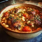 Nahaufnahme des fertigen Easy Chicken Cassoulet mit knusprigen H&auml;hnchenkeulen, wei&szlig;en Bohnen und Kirschtomaten.