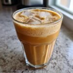 Nahaufnahme eines k&uuml;hlen Frapp&eacute; mit cremigem Schaum und Eisw&uuml;rfeln in einem Glas.