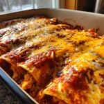 Nahaufnahme von gebackenen Chicken Enchiladas in einer Auflaufform, bedeckt mit roter Sauce und geschmolzenem Cheddar-K&auml;se.