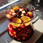 Nahaufnahme von Festive Christmas Sangria in einem Glaskrug mit Orangen, &Auml;pfeln, Zimtstangen und Sternanis.