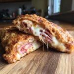 Aufgeschnittene Fried Pizza Sandwiches mit geschmolzenem K&auml;se und Schinken, die auf einem Holzbrett liegen.