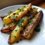 Nahaufnahme von knusprigen Garlic Butter Roasted Parsnips, garniert mit frischer Petersilie auf einem wei&szlig;en Teller.