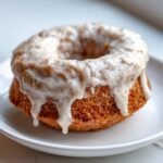 Nahaufnahme eines gebackenen Zimt-Donuts mit dicker, tropfender Vanilleglasur.