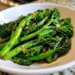 Nahaufnahme von leuchtend gr&uuml;nem, gebratenem Knoblauch-Broccolini in einer wei&szlig;en Sch&uuml;ssel.