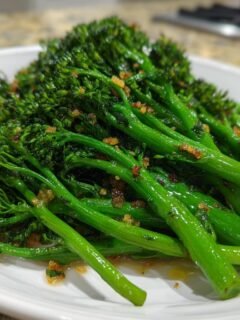 Nahaufnahme von leuchtend grünem, gebratenem Knoblauch-Broccolini mit Knoblauchstücken auf einem weißen Teller.