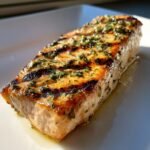 Nahaufnahme eines saftigen, gegrillten Mahi Mahi Filets mit deutlichen Grillstreifen und gr&uuml;nen Kr&auml;utern.