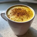Nahaufnahme eines cremigen Golden Milk Latte in einer wei&szlig;en Tasse, bestreut mit Zimt.