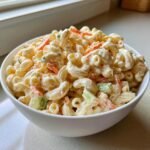 Nahaufnahme von cremiger Hawaiian Macaroni Salad mit Makkaroni, Karotten und Sellerie in einer wei&szlig;en Sch&uuml;ssel.